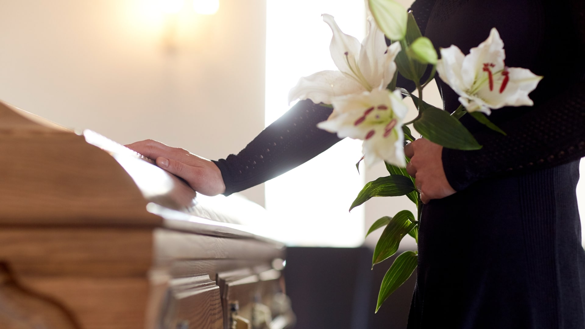 How Long Is a Funeral? Man standing with white lillies at a closed casket practicing proper funeral etiquette