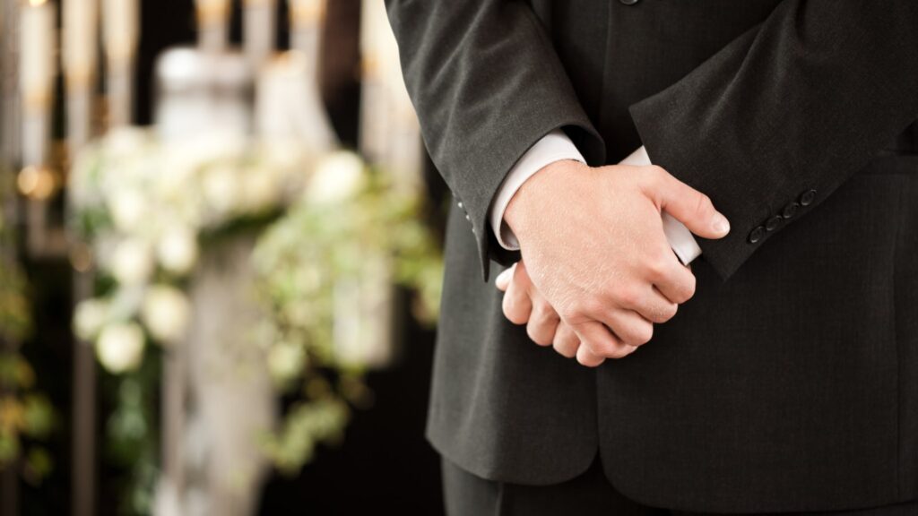 Man standing in proper funeral attire with hands over one another