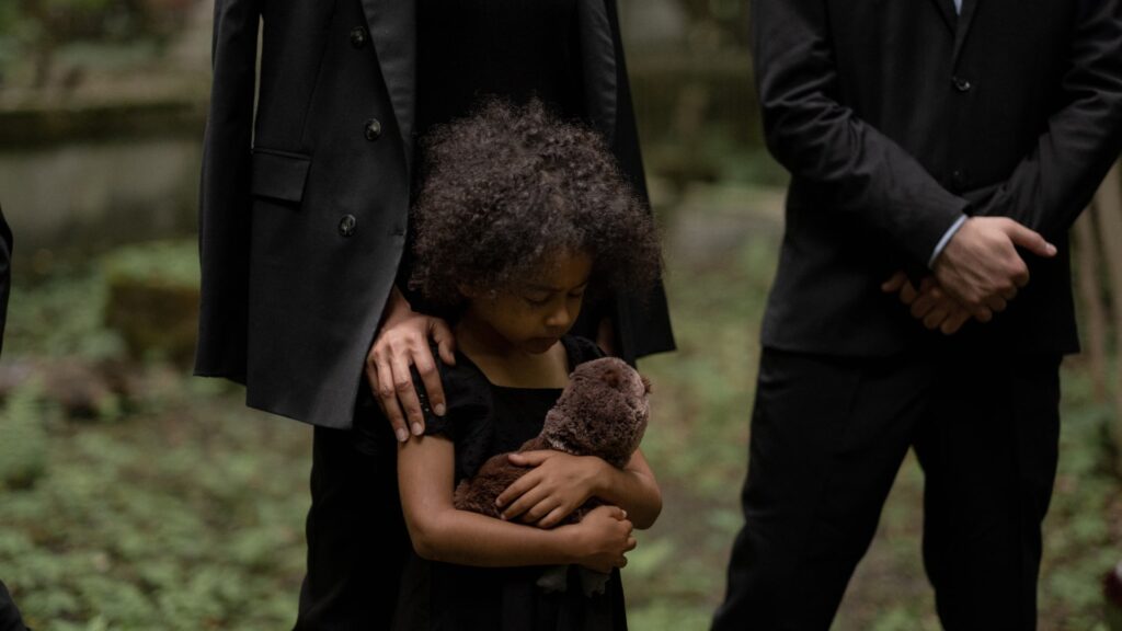 young girl wearing a black dress and holding her teddy bear