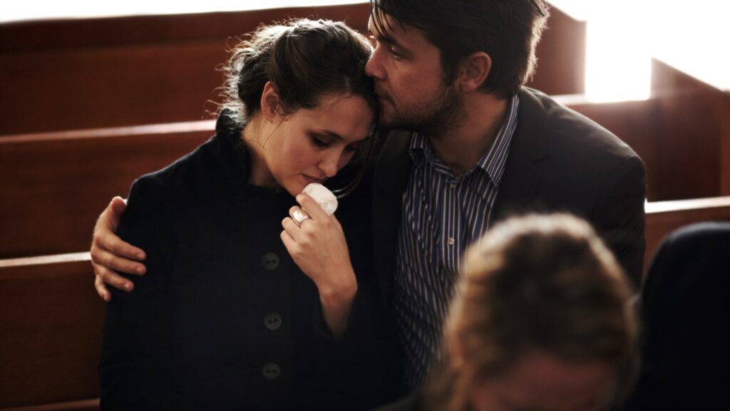 Man dressed in proper funeral attire with his arm around sad woman knowing what to wear to a funeral